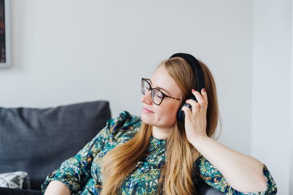 Side view of a young woman daydreaming with closed eyes while listening to relaxing music through black over-ear headphones at home